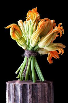 yellow flowers are in a wooden vase on a black background with the stems still attached