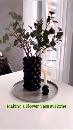 a white table topped with a vase filled with black beads and a candle next to a window