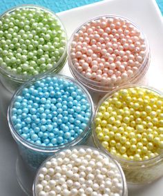 four small bowls filled with colorful beads on top of a white plate and blue table cloth