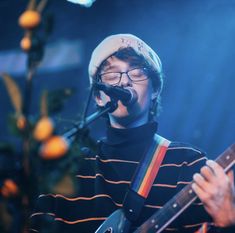 a man with glasses and a striped shirt playing guitar in front of a microphone on stage