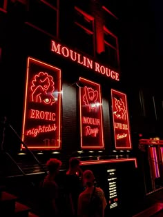 people are standing in front of the moulin roulee neon sign at night