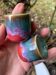 two handmade coffee mugs sitting in the palm of someone's left hand