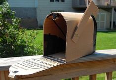 an open cardboard mailbox sitting on top of a wooden fence post in front of a house