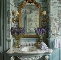 a bathroom with blue walls and wallpaper has a mirror, sink, and flowers in vases