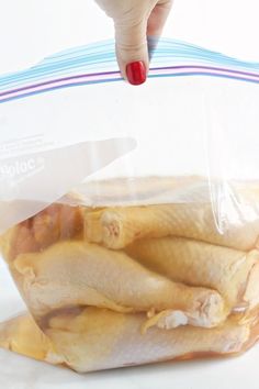 a woman's hand reaching into a plastic bag filled with raw chicken