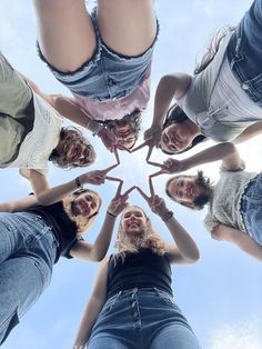 four girls standing in a circle with their hands together and looking up at the sky