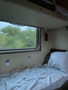 a bed with white sheets and pillows in a small room next to a large window