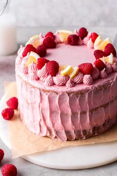 a pink cake with raspberries and lemons on top sits on a plate