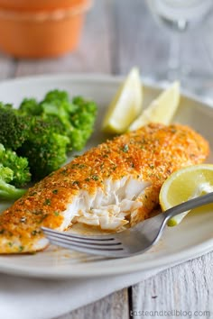 a white plate topped with fish next to broccoli and lemon wedges on top of a table