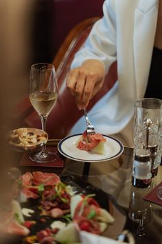 a person is eating at a table with wine glasses and food on the plates in front of them