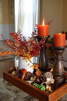 two candles are sitting on a tray with autumn decorations in front of a window,