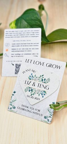 two tags with leaves on them sitting next to some flowers and greenery in the background