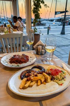 two plates of food on a table with wine glasses and people sitting in the background