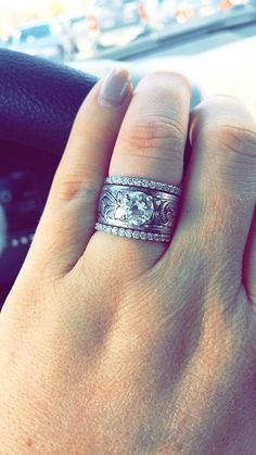 a woman's hand with a wedding ring on her left and a car steering wheel in the background