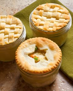 three small pies sitting on top of a green napkin next to each other in glass jars