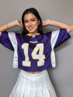 a woman wearing a purple and white football uniform with her hands on her head while standing in front of a gray wall