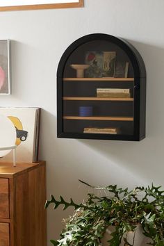 a wall mounted shelf with books on it next to a potted plant and framed pictures