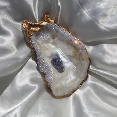 an agate shell with pearls on it sitting on a white satin surface, surrounded by gold trimmings