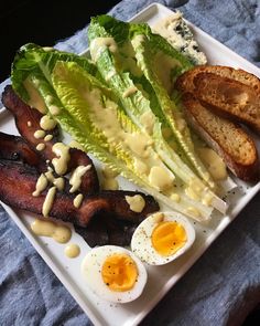 a white plate topped with bacon, lettuce and eggs next to toasted bread