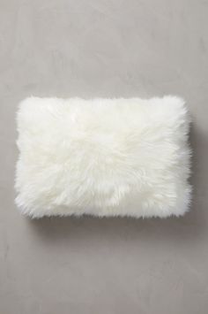 a white furry pillow sitting on top of a gray floor next to a grey wall