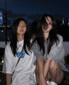 two young women sitting next to each other in front of a street sign at night