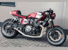 a red and black motorcycle parked on top of a brick road next to a building