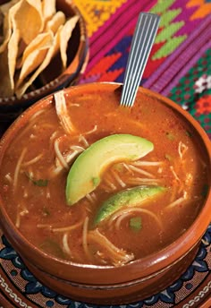 a bowl of soup with an avocado and tortilla chips