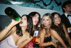 four women are posing for the camera with drinks in their hands and one is holding a bottle