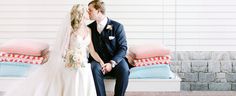 a bride and groom sitting on a bench in front of a house with pillows behind them