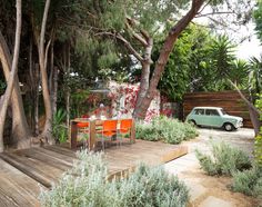 an outdoor dining area with wooden decking and orange chairs, surrounded by greenery