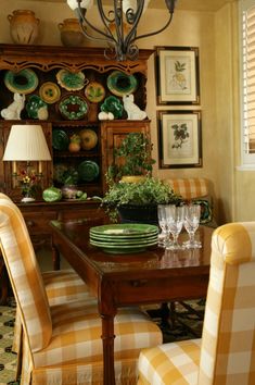 a dining room table with yellow chairs and green plates on the wall above it, in front of an old china cabinet