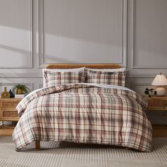 a bed with plaid comforter and pillows in a room next to a lamp on a table