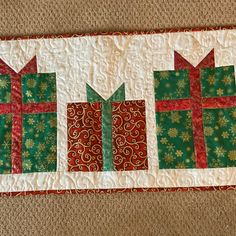 a quilted table runner with three christmas presents on the front and two red bows on the back