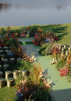 a green course surrounded by lots of flowers next to a body of water with trees in the background