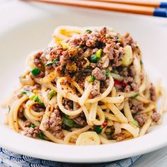 a white bowl filled with noodles and meat on top of a table next to chopsticks