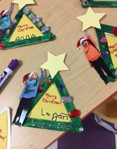 three children are standing in front of christmas tree decorations on a table with markers and crayons