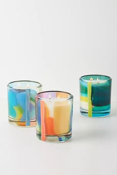 three colorful candles sitting next to each other on a white surface with one candle in the middle