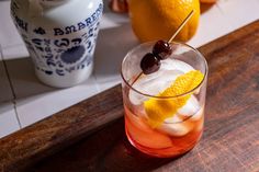 an orange drink with ice and cherries on the rim next to two lemons