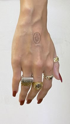 a woman's hand with rings on it and a small circle tattoo on the middle finger