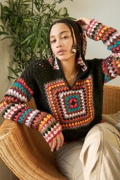 a woman sitting in a chair wearing a sweater with colorful crochet on it