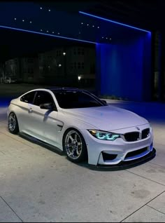 a white car parked in front of a building at night with blue lights on it