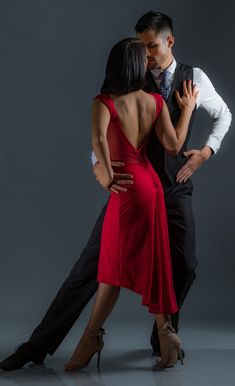 a man and woman in formal wear dance together against a gray background with their arms around each other