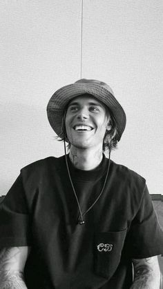 black and white photograph of a man wearing a fedora sitting in front of a wall