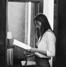 a woman standing in front of a mirror reading a book