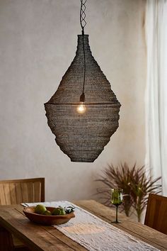 a wooden table topped with a bowl of fruit and a light fixture hanging from the ceiling