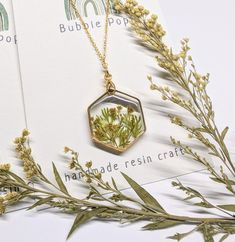 a close up of a plant in a glass jar on a chain necklace next to some flowers