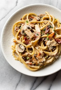 a white bowl filled with pasta covered in mushrooms and sauce on top of a marble table