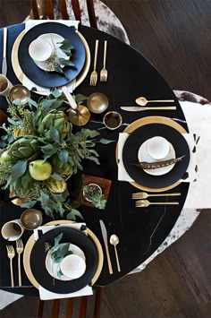 the table is set with black and gold plates, silverware, and greenery