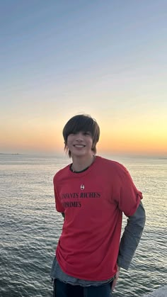 a young man standing on the edge of a pier next to the ocean at sunset