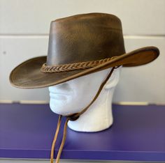 This hat is crafted from oily distress color with full grain Leather and features leather braided band. It includes a sweatband on the inside for comfort. Made with handcrafted leather for both men and women.  Its available in both brown and black natural leather colors.  You can make your own style as the brim of the hat is easily shapable. It is unlined on the inside. The wide brim of this leather hat provides shade in the sun.  It is made from 100% pure leather. The hat is approximately 3" br Brown Waxed Brimmed Hats, Brown Waxed Finish Hats, Rugged Distressed Brown Leather Hat, Distressed Brown Leather Brimmed Hat, Rustic Leather Hat Bands For Outdoor, Rugged Leather Hats For Western-themed Events, Leather Hats For Country Events In Distressed Brown, Leather Distressed Brown Hats For Country Events, Distressed Brown Leather Hats For Country Events